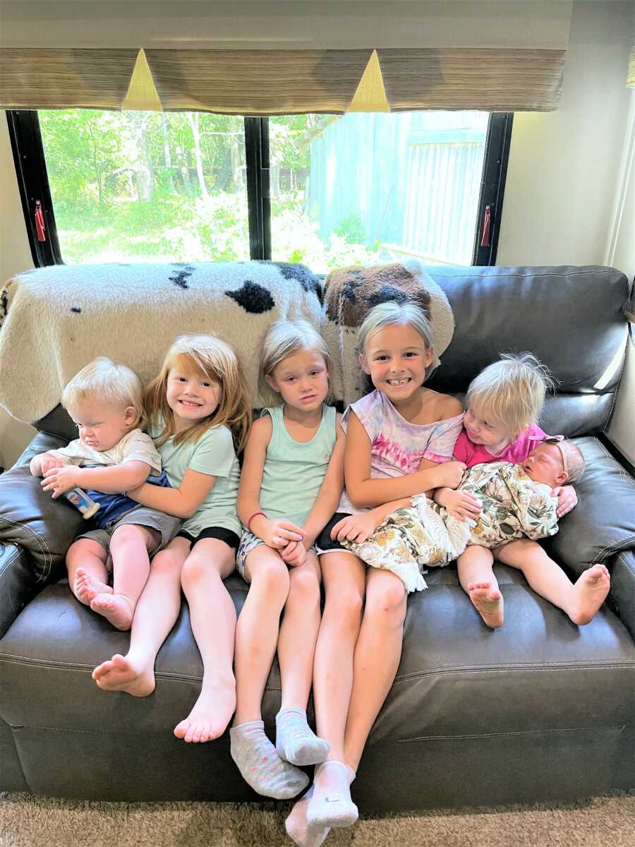 6 kids sitting on a couch inside of a camper house smiling 