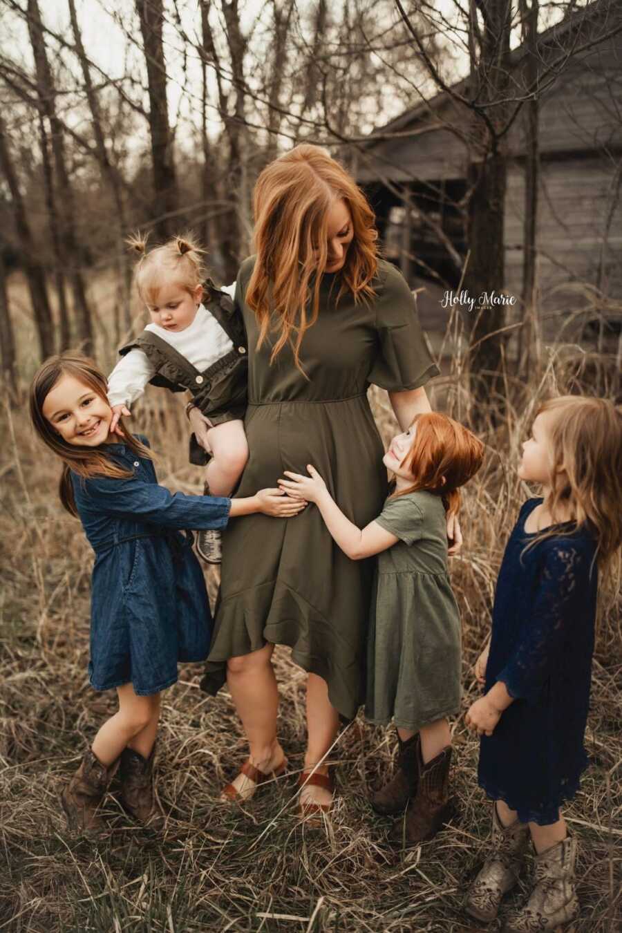 pregnant mom holding her baby daughter with her older 3 daughters hug her 