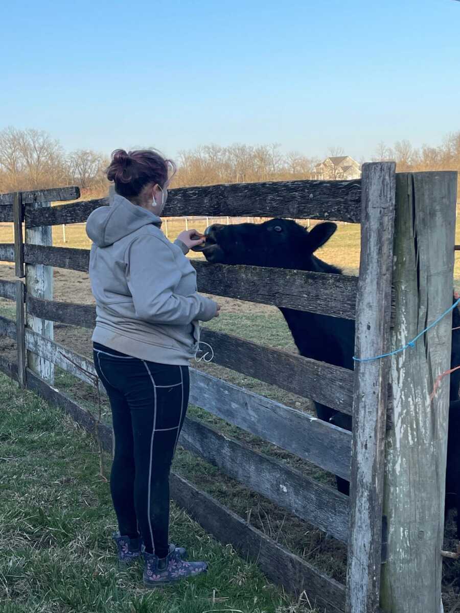 Teen foster girl feeds a cow through a wooden fence.