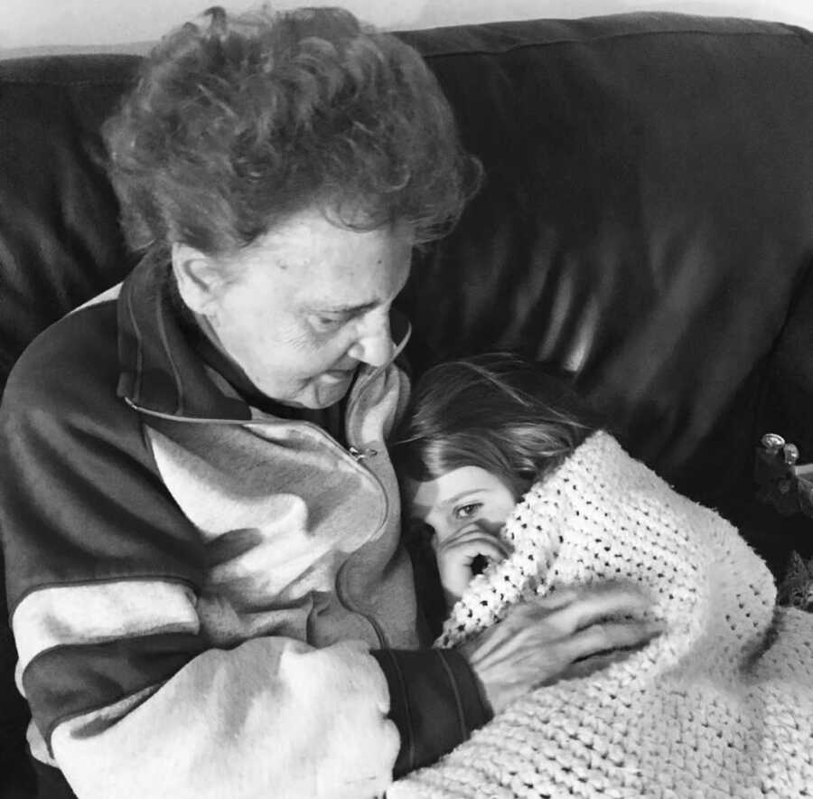 Grandma holds her granddaughter while they snuggle on the couch together