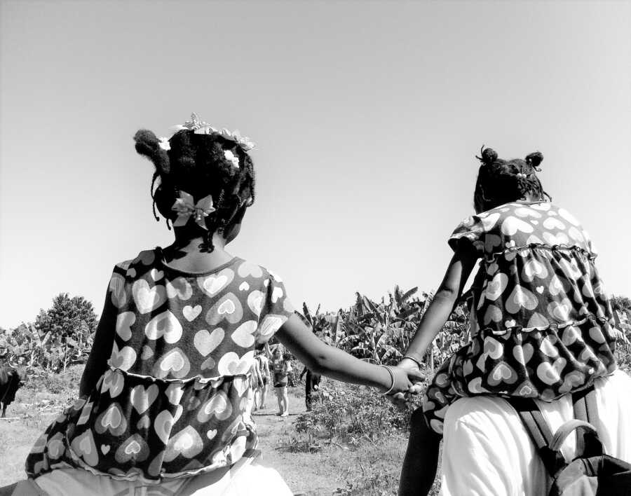 Two young Haitian sister holding hand while riding on the shoulders of two adults 