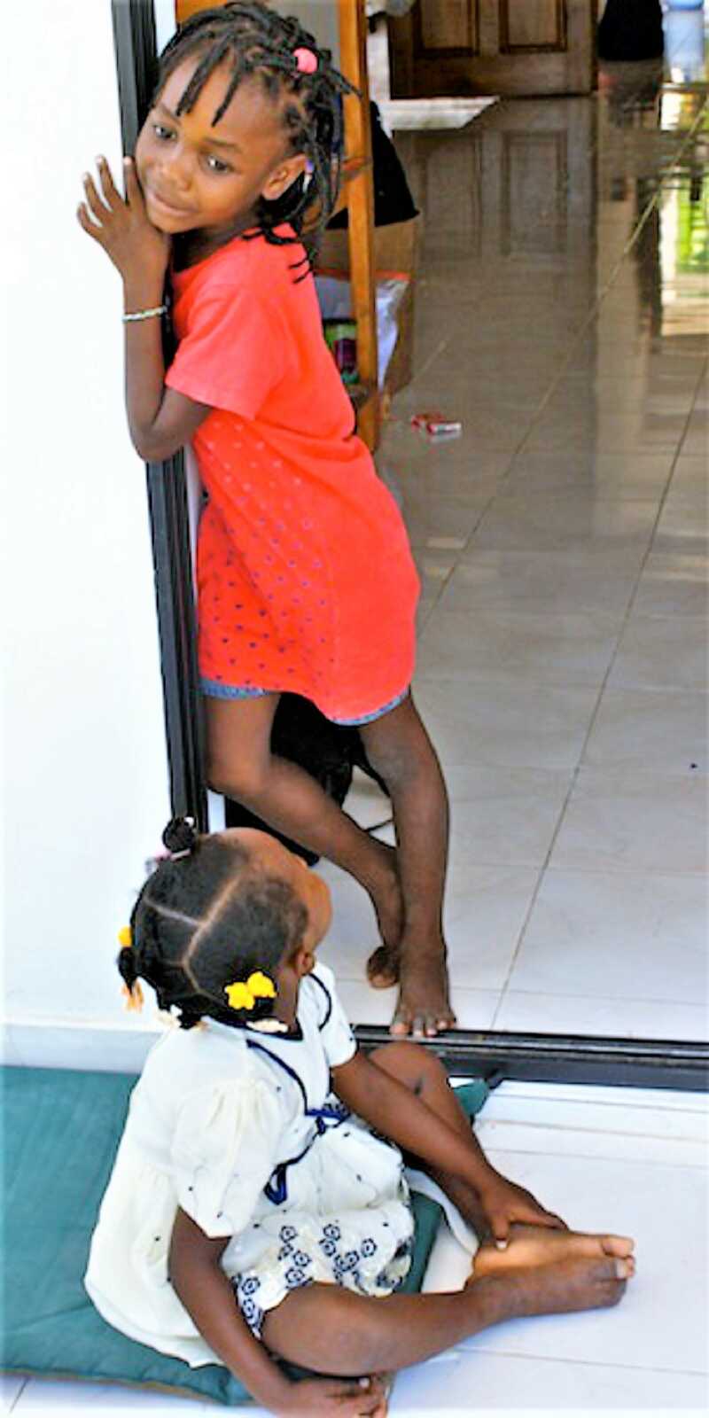 Two Haitian sisters hanging out at the front door of their house in Haiti