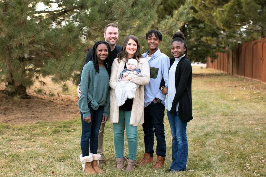 Mom and dad posing next to their three adoptive son and daughter from Haiti while also holding their biological baby 