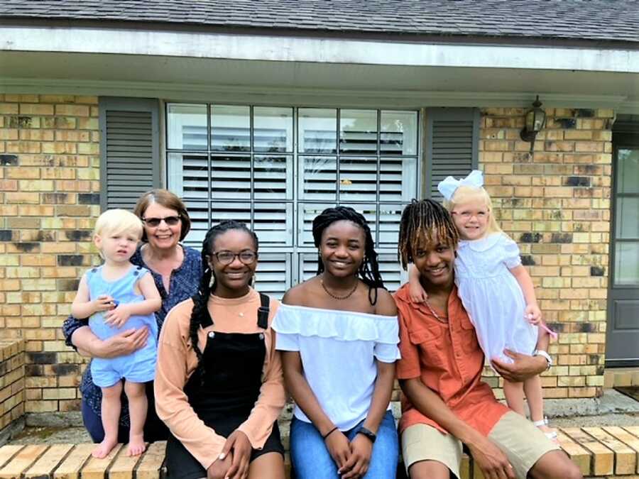 Three older siblings sitting next to their two toddler sister and baby brother at the front of their house 