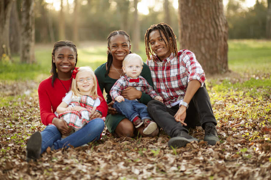 Three older siblings sitting in the woods holding their two younger siblings 