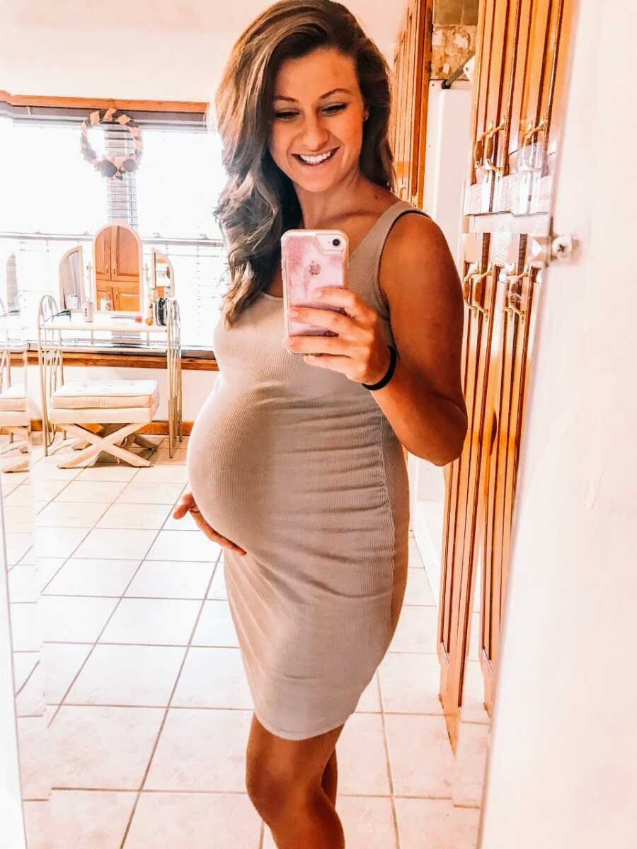 Woman pregnant with her second child takes mirror selfie while wearing a skin-tight tan dress