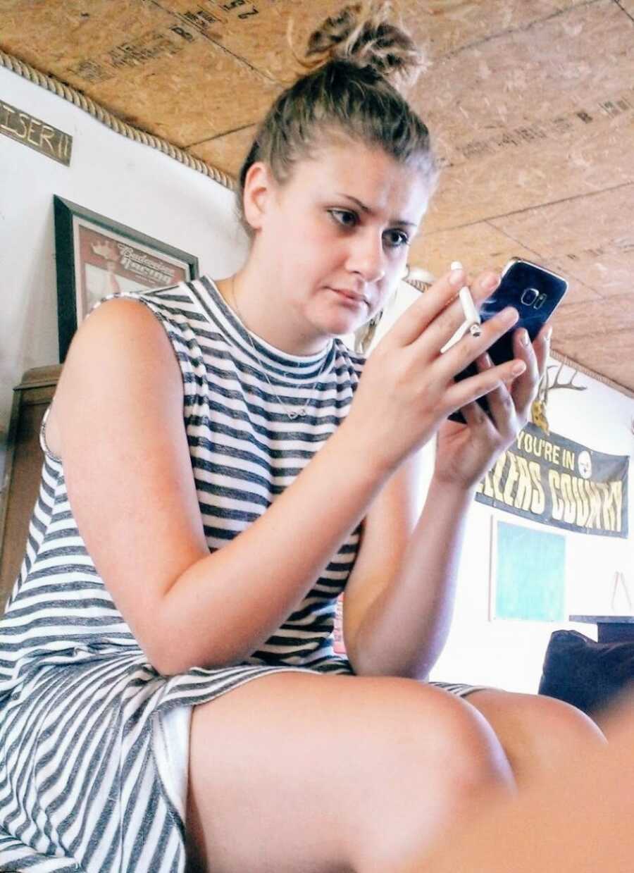 Woman in a striped dress looks angry while smoking a cigarette and scrolling on her phone