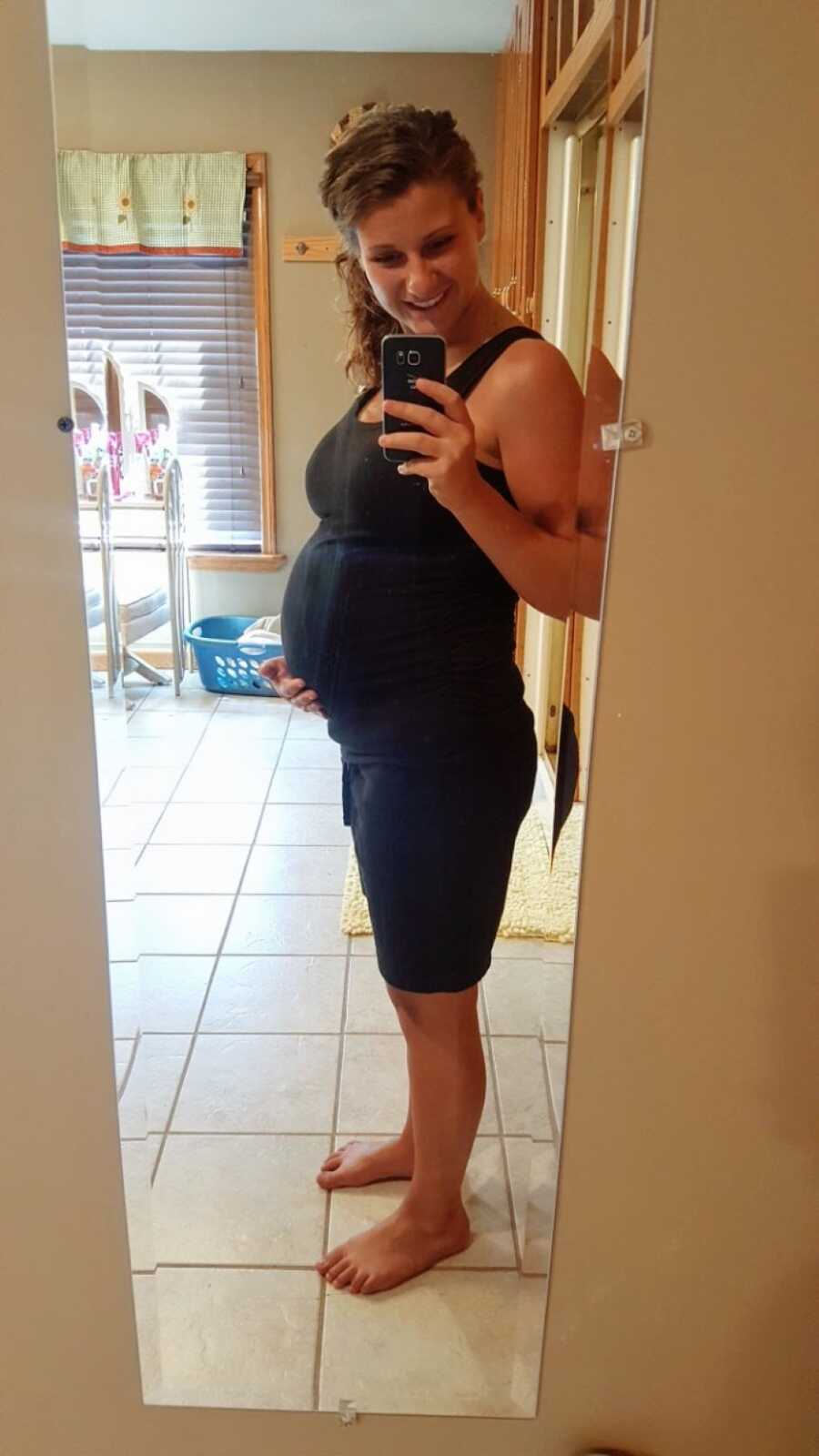 Mom pregnant with her first child takes a mirror selfie in a black skin-tight dress