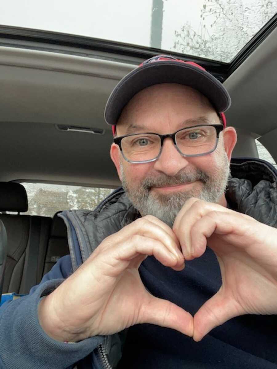 man making heart with hand while sitting in care