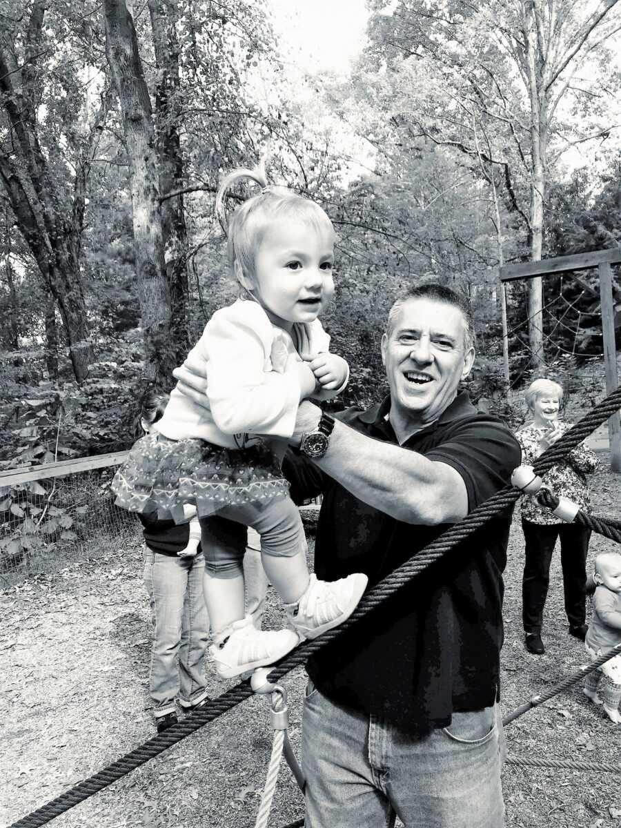 Step-grandpa holding step-granddaughter at the park 