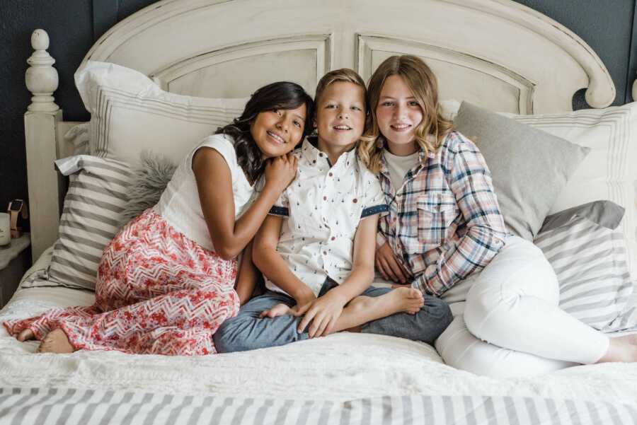 three children sitting on their parents bed