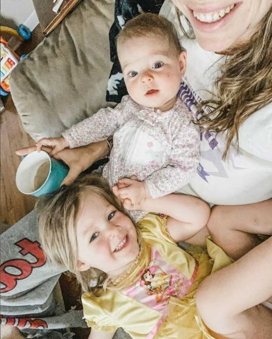 Mom cuddles with her two daughters on the couch while drinking coffee