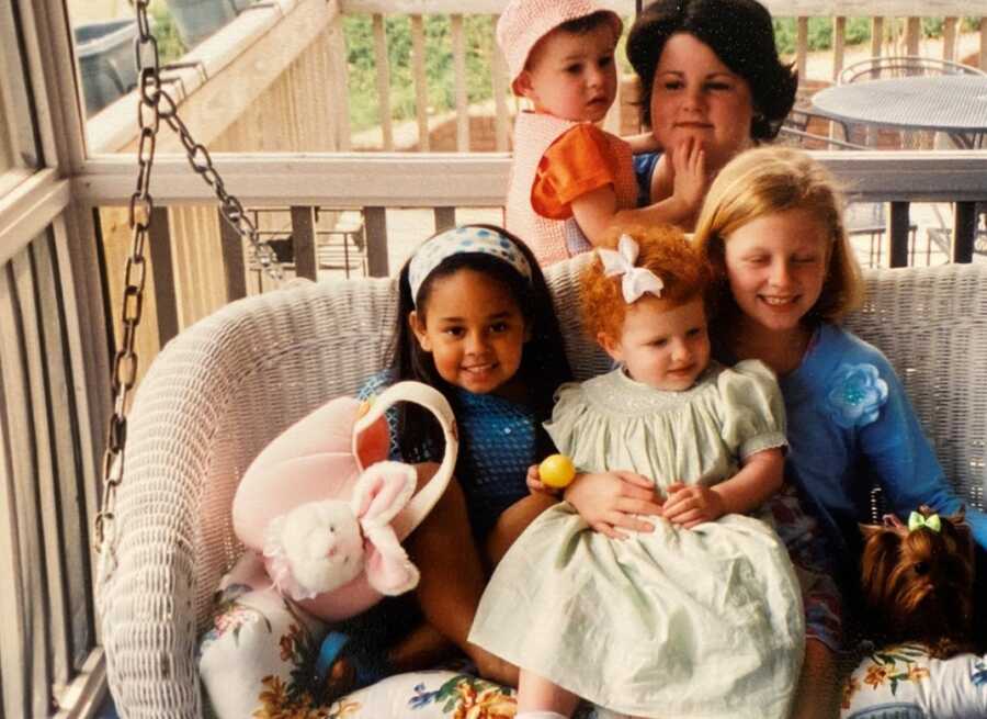 Young girl takes picture sitting on porch swing with cousins as she stays with them while her mom goes to rehab.