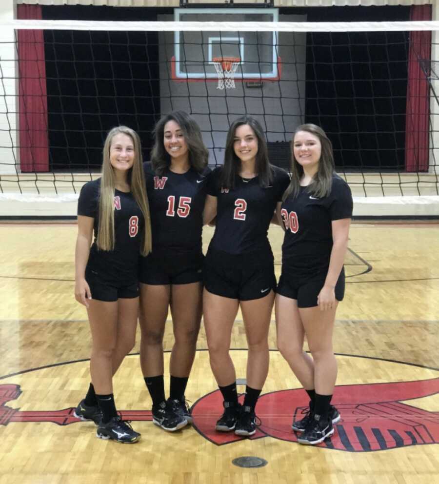Foster teen takes picture with fellow volleyball teammates standing on the court in front of the net.