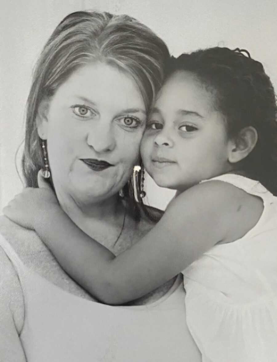 Biological mom takes picture with young daughter wrapping arms around her neck.