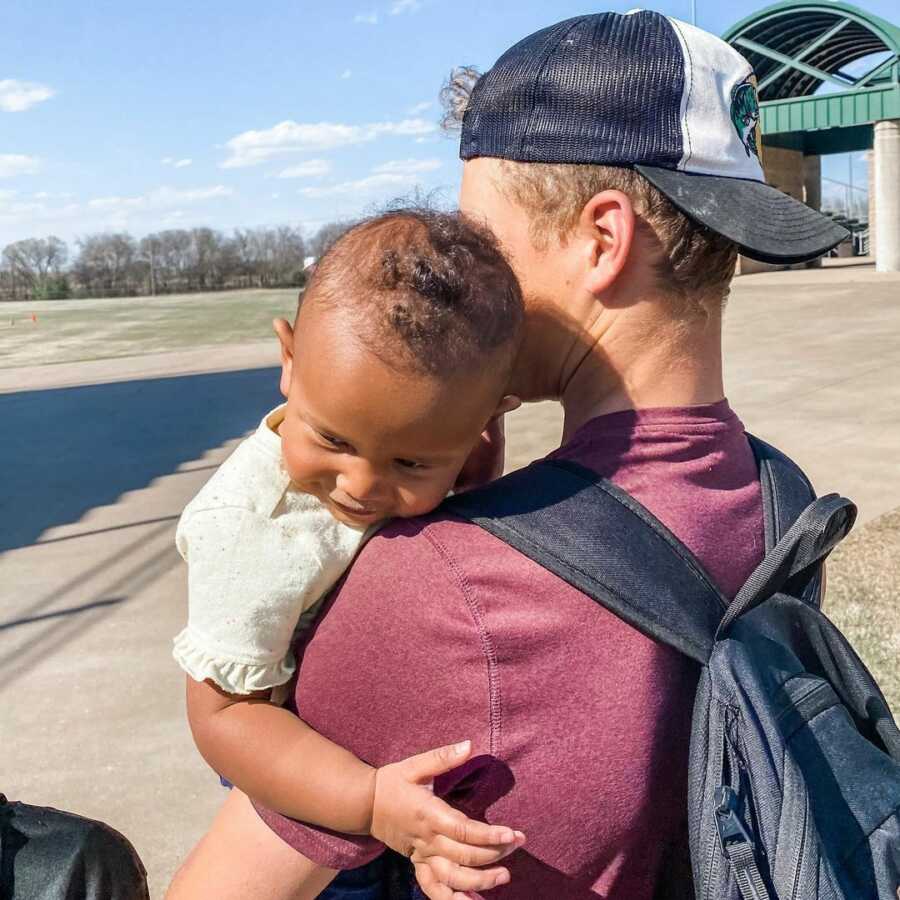man holds baby over his shoulder