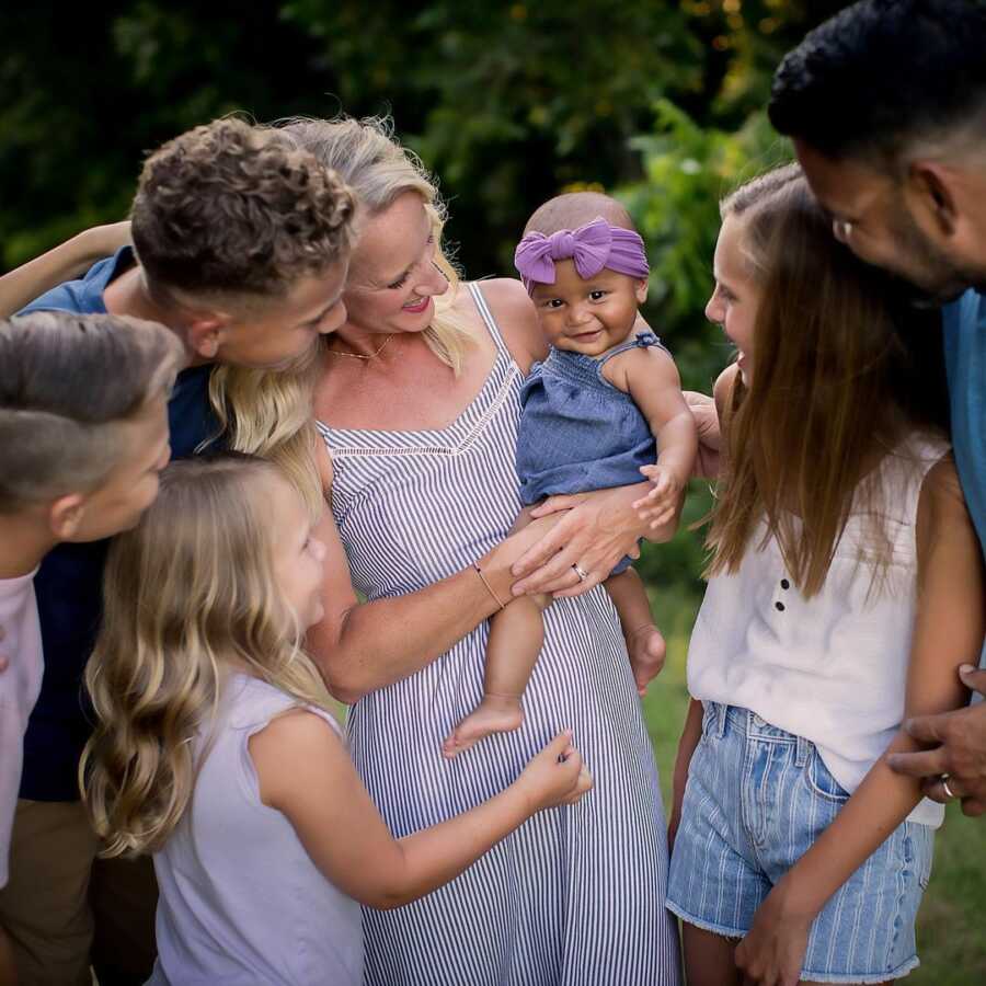 family stands around mom who is holding their adopted daughter/sibling