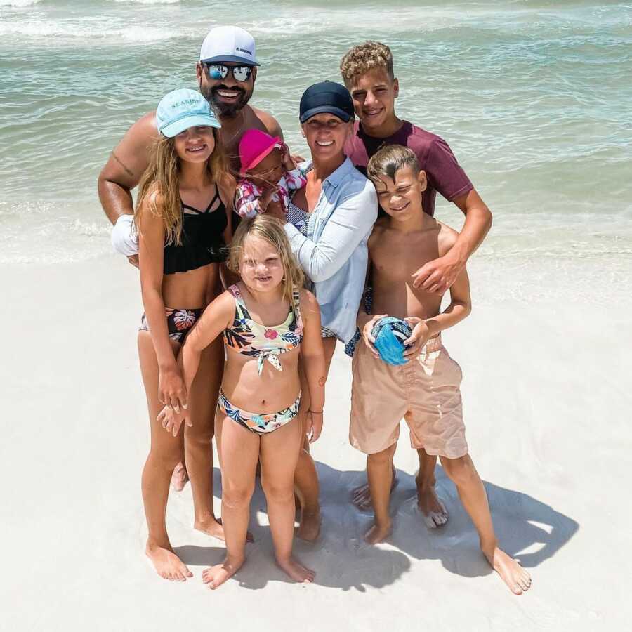 family stands on the beach together in front of the water