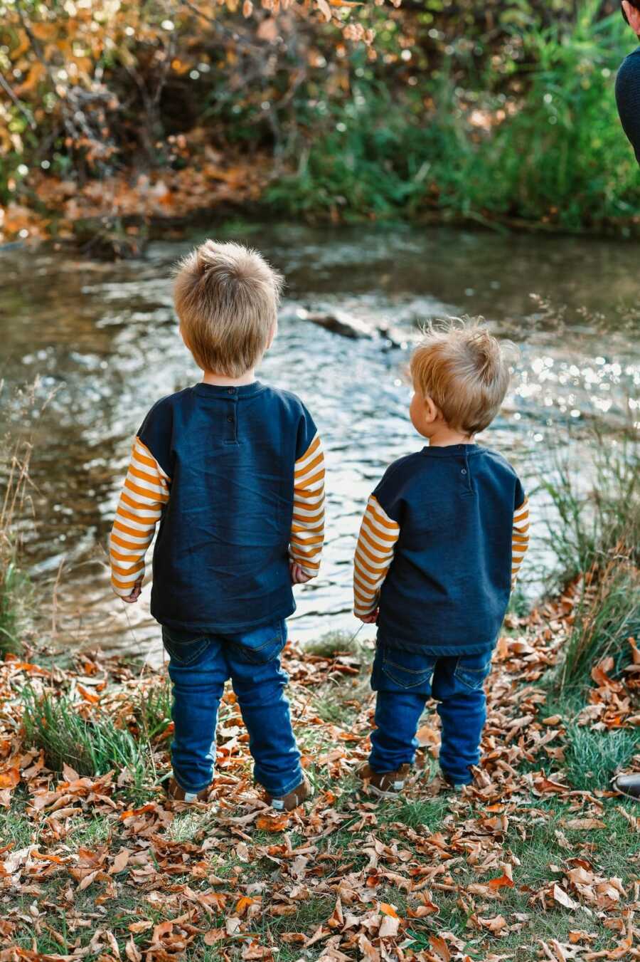 Young brothers stand side by side facing creek.