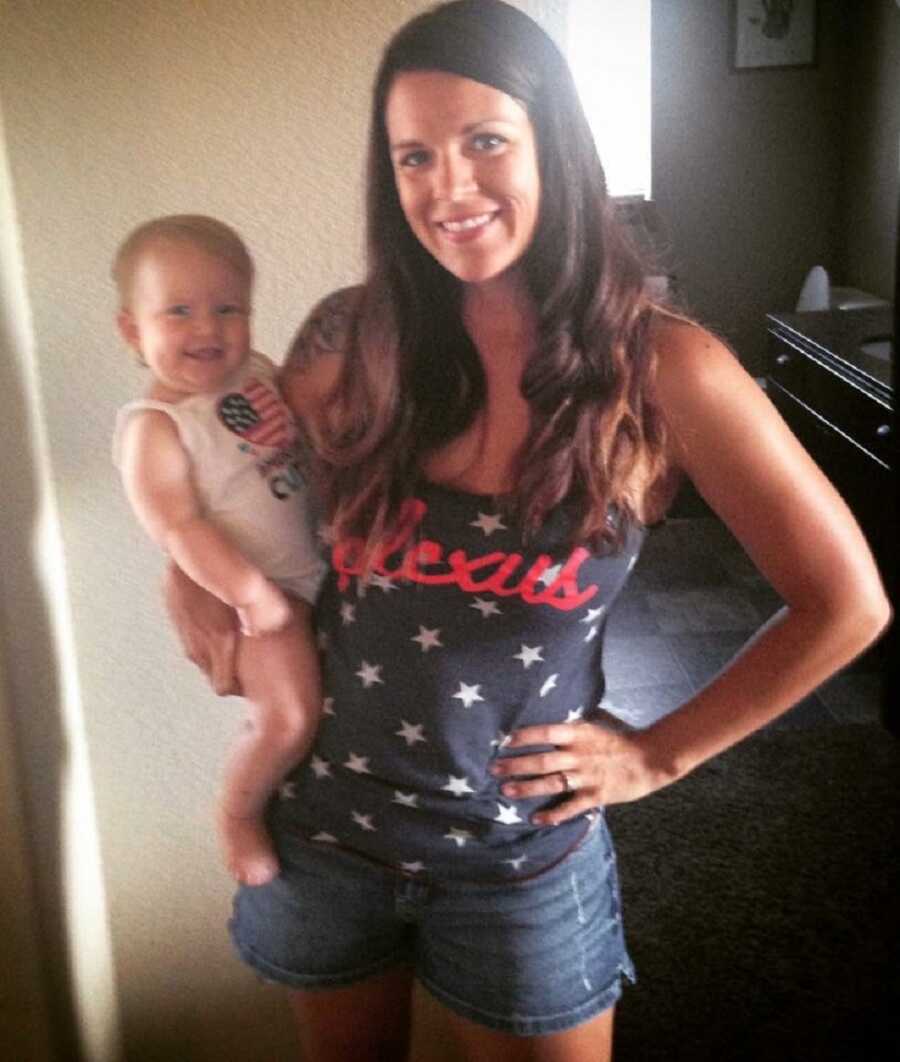 Young mom wearing Plexus tank top holds baby girl on her hip.