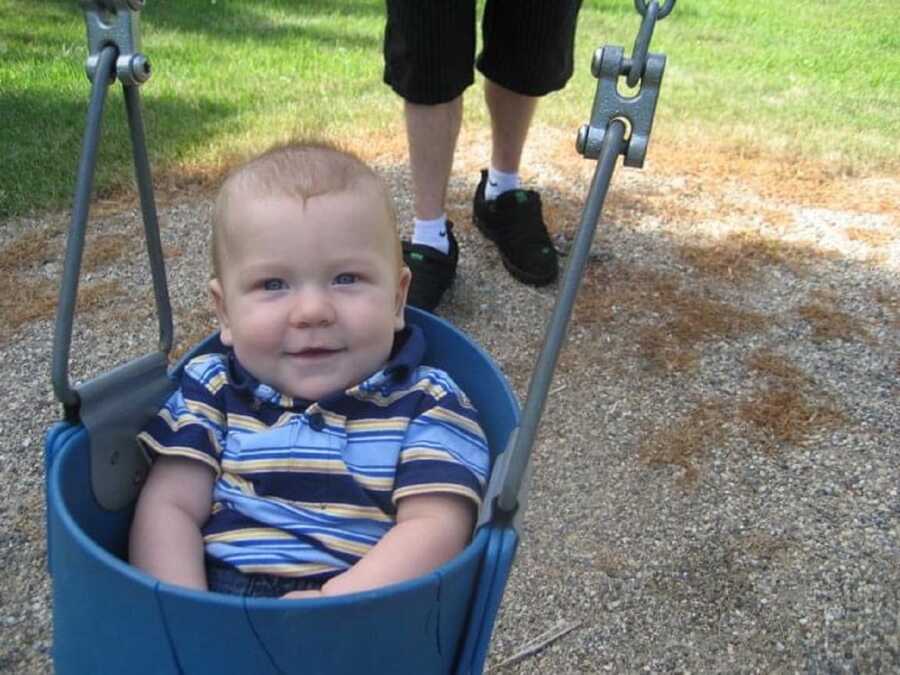 Baby boy wearing striped polo shirt happily swings at the playground.