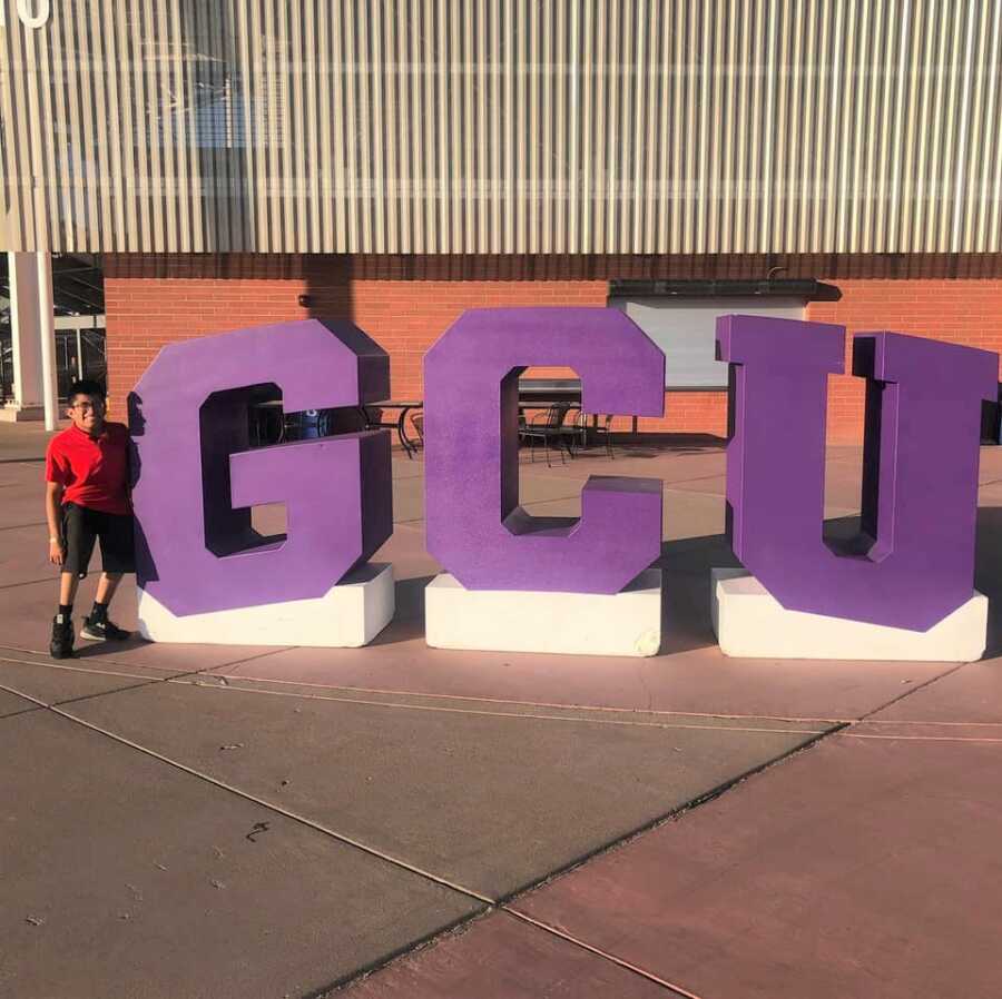 Young man takes picture standing next to GCU letters at Grandy Canyon University.