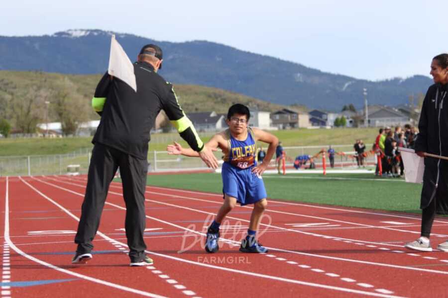 Young man high fives coach as he competes in high school track meet.