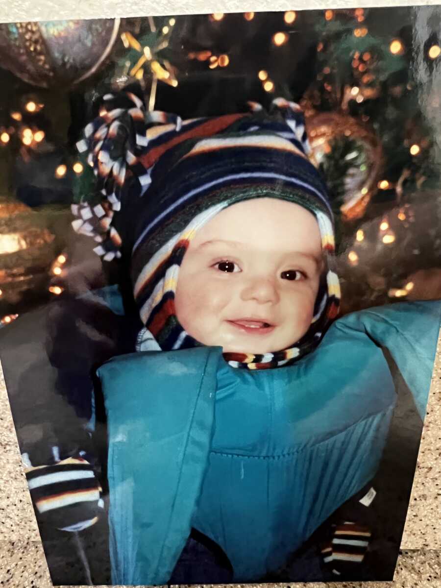 Young baby boy wears blue winter coat and striped beanie.