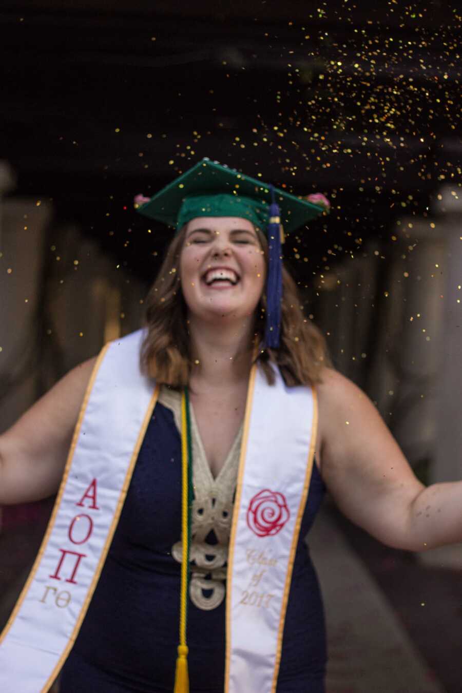 College graduate smiles under gold glitter wearing her sorority stoll