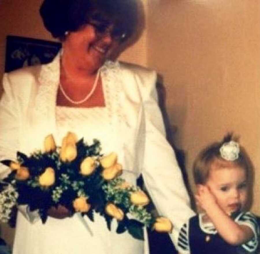 A woman in a wedding dress smiles down at a toddler girl