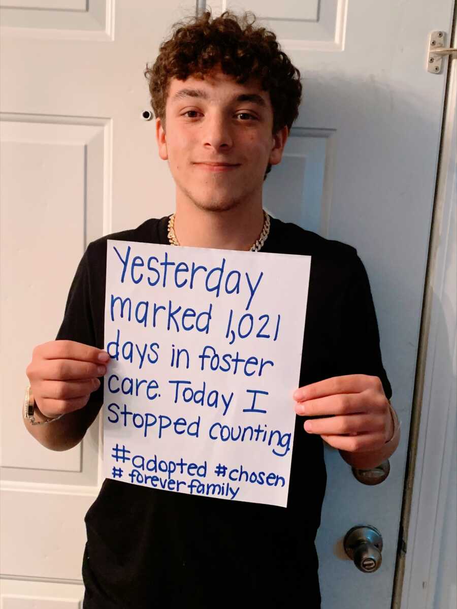 A boy holds up a sign stating that he has been adopted