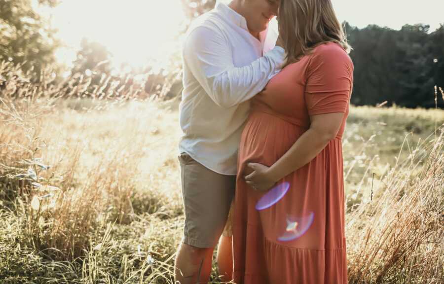 husband holds pregnant wife's face as they stand close to one another