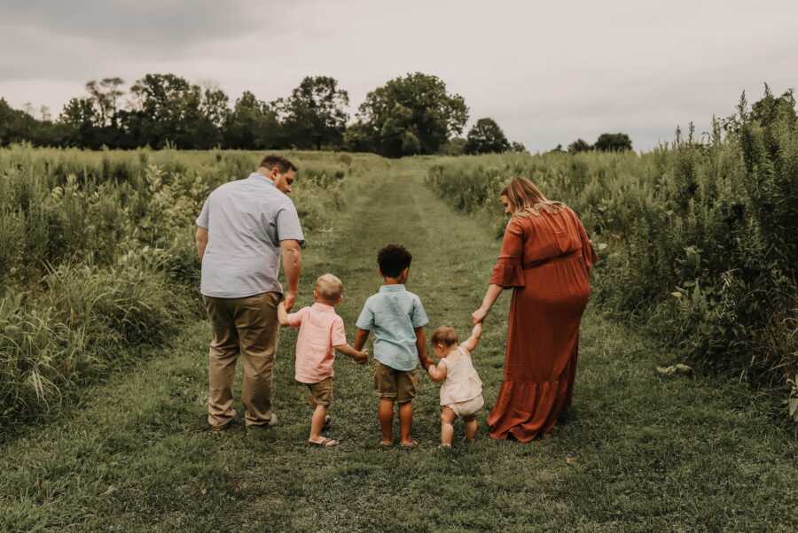 family of four stands hand in hand walking through a field