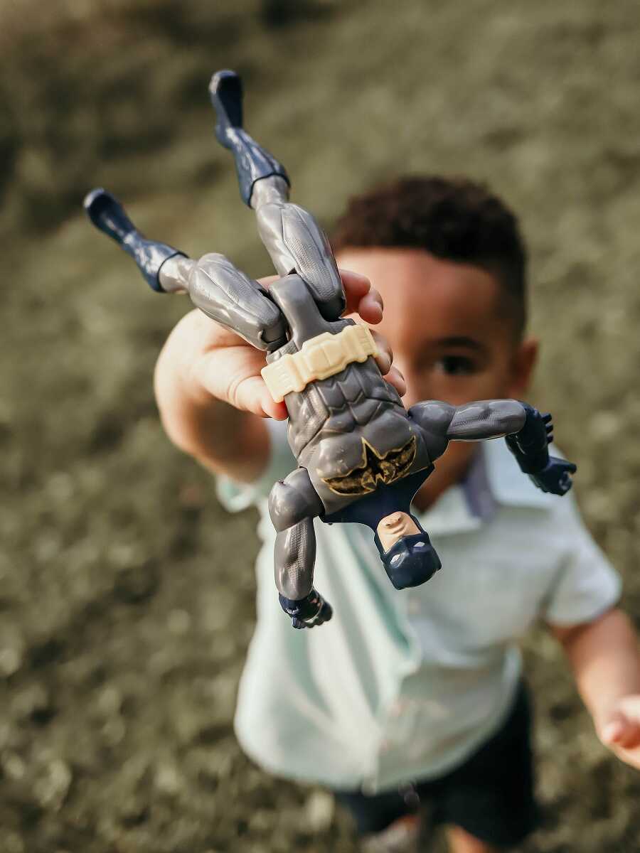 young black boy in foster care holds up batman action figure in front of his face