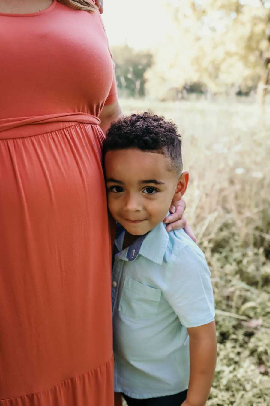 young boy stands close to his adoptive mothers side