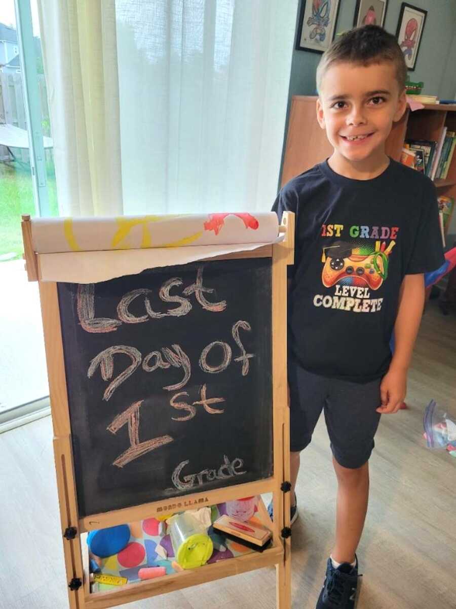 young boy stands next to chalkboard saying "last day of 1st grade"