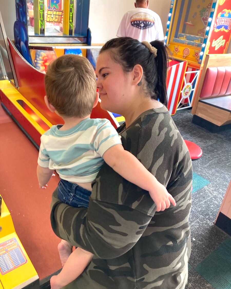 mom holds her younger son while playing ski ball