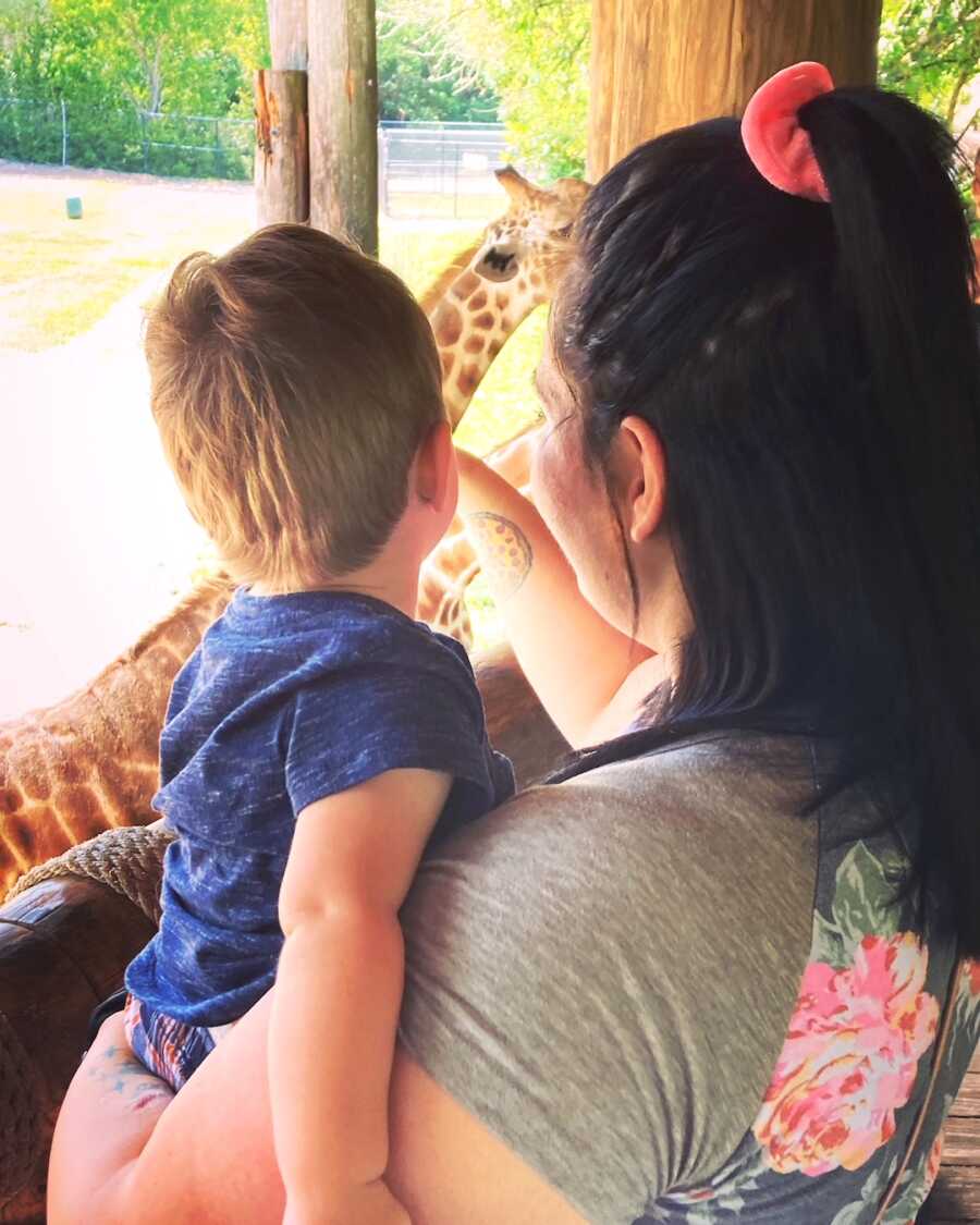 mom holds her son while they feed a giraffe