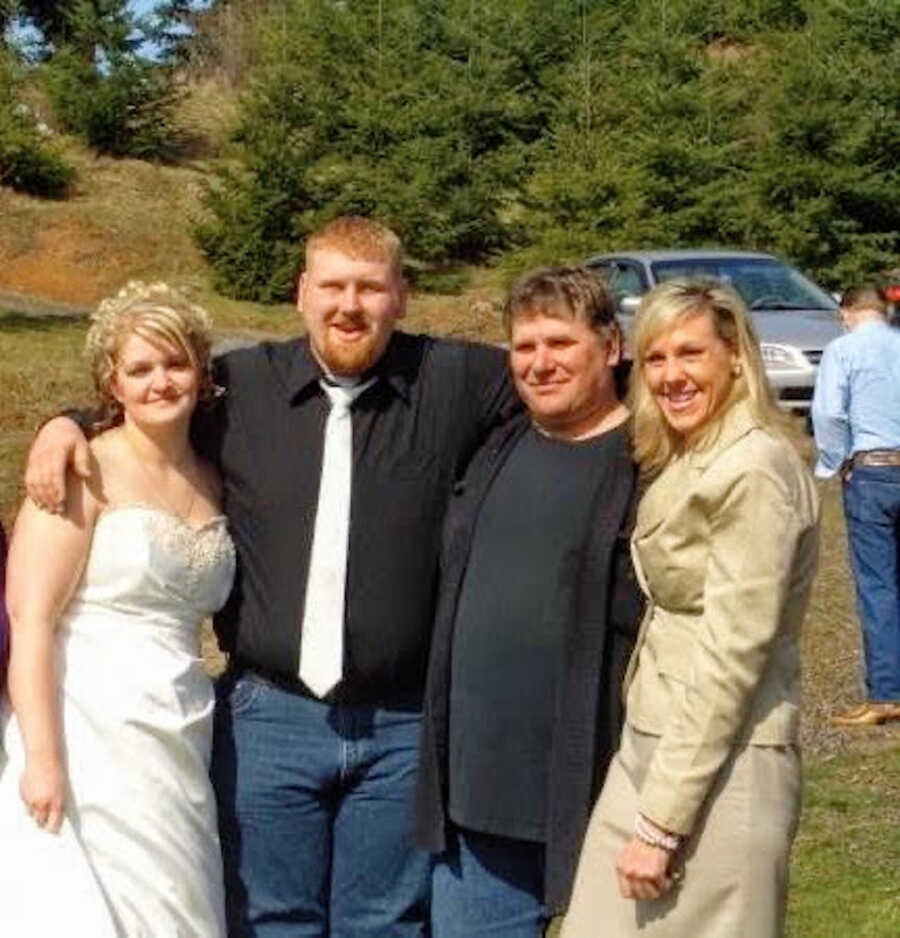 Three people pose with a woman in a wedding dress