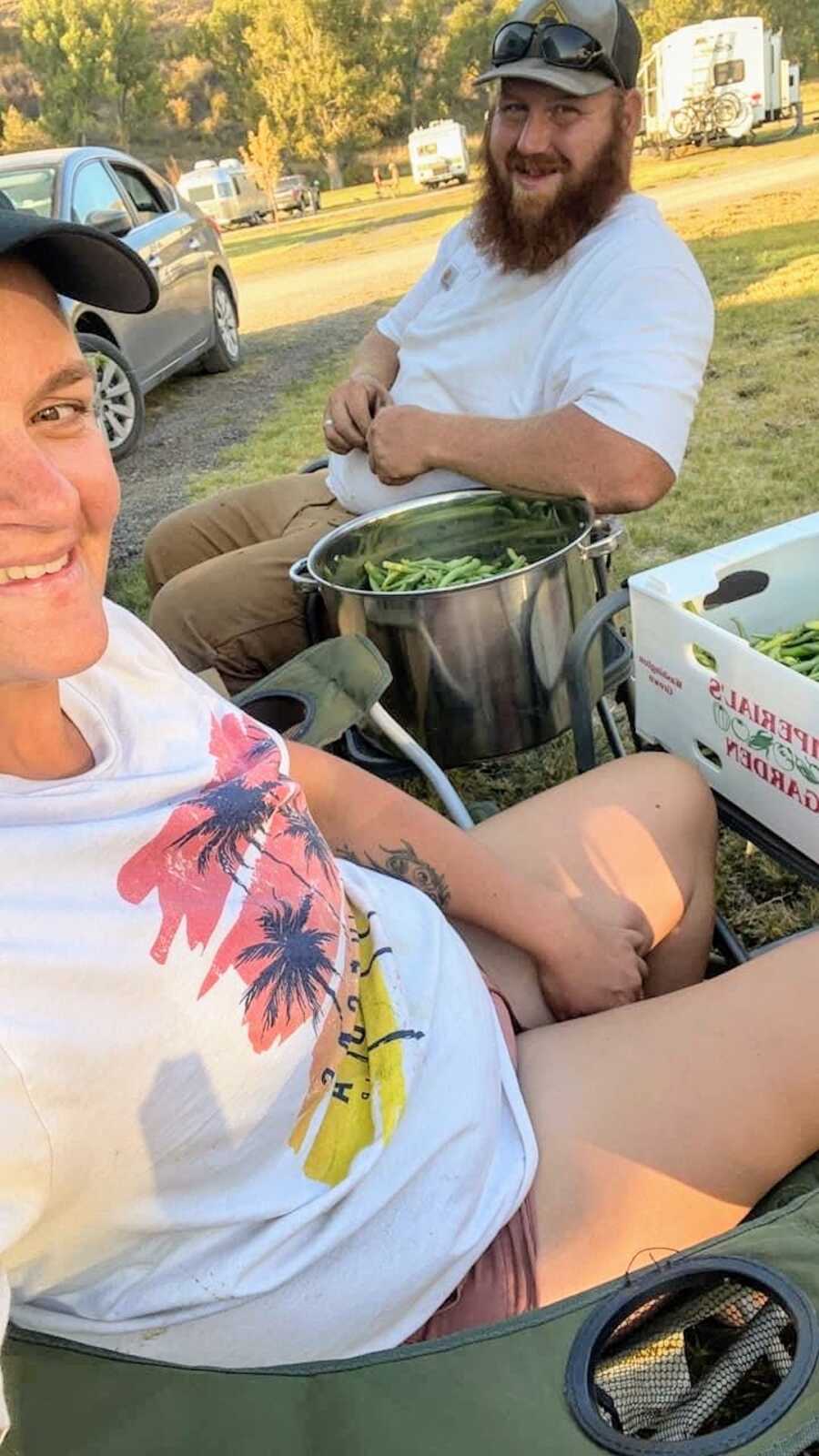 A man and woman sit next to a pot of vegetables