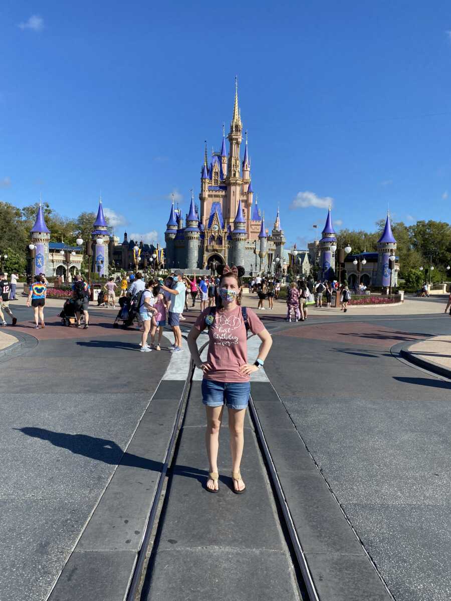 Young widow stands in front of Disneyland castle and takes picture by herself.