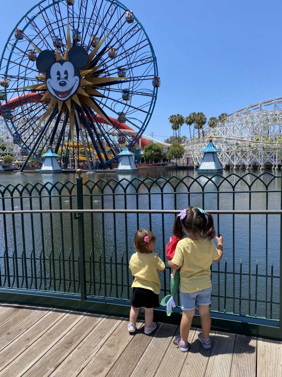 Foster sisters stand behind fence looking at the Mickey Mouse roller coaster at Disneyland.