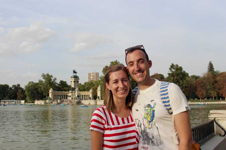 Husband and wife take smiling picture standing together on vacation.