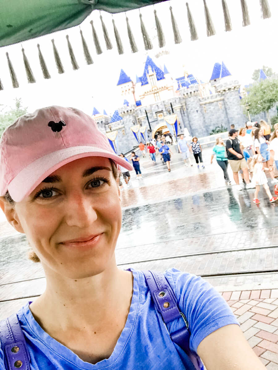 Young widow wearing pink Disney hat takes a selfie at Disneyland.