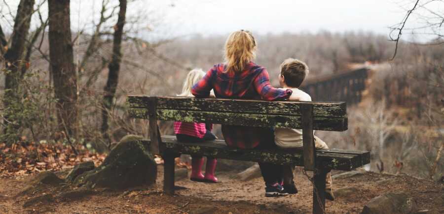 mother sits on a bench with her two children at her side