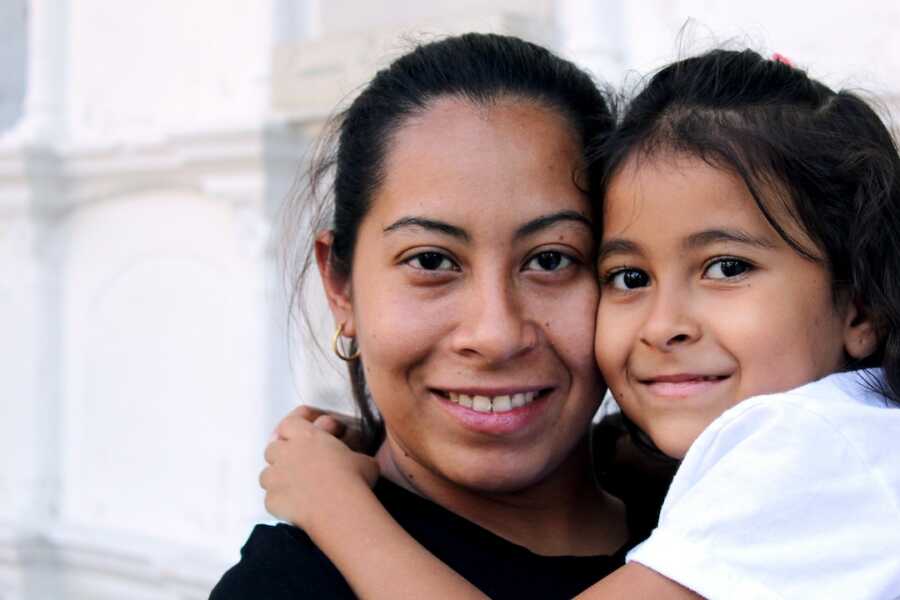 mother holds her daughter close to her face, both smile