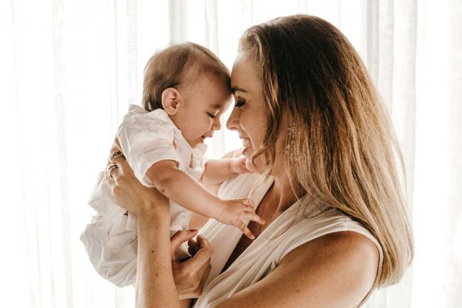 mom holds her baby up close to her face and smiles