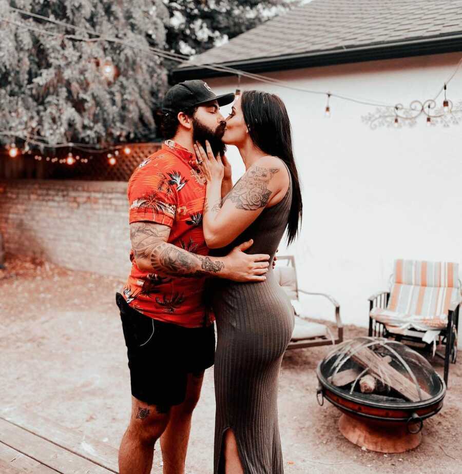 Husband and wife hold each other as they kiss in backyard patio space.