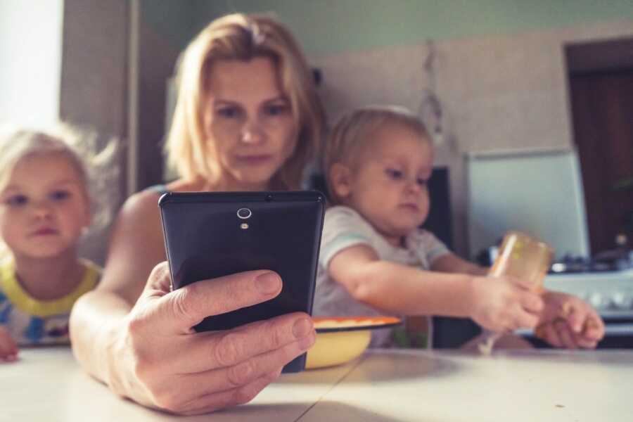 mother sits at table on her phone while having child on her lap