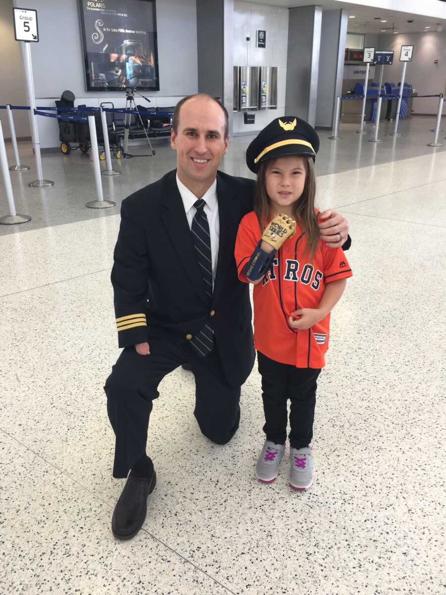 Pilot with limb difference crouches down next to little girl missing a hand and takes picture letting her wear his pilot hat.